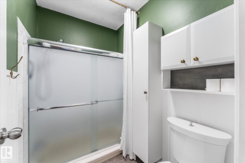 The bathroom features a shower with frosted glass doors, a white toilet, and white cabinetry offering storage solutions - 2626 49 Street, Edmonton, AB - Indoor Photo Showing Bathroom
