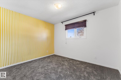 The room features a decorative accent wall with vertical yellow stripes, soft gray carpeting, and a window with blinds - 2626 49 Street, Edmonton, AB - Indoor Photo Showing Other Room