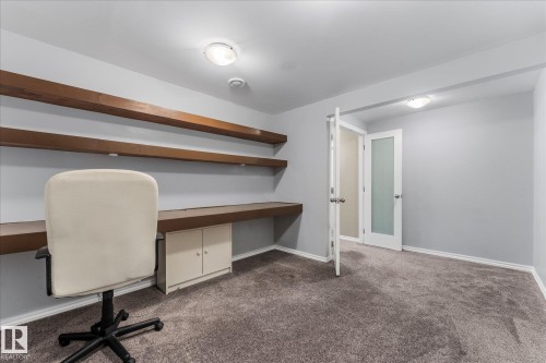 This room features built-in wooden shelving, a desk area with integrated cabinetry, and soft grey carpeting - 2626 49 Street, Edmonton, AB - Indoor Photo Showing Office