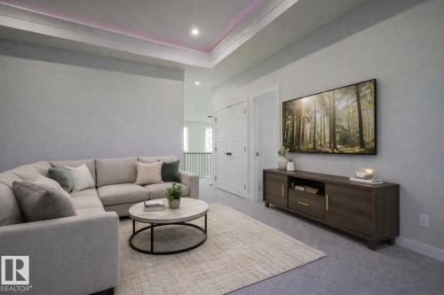 This inviting living area features soft carpeting, a recessed ceiling with ambient lighting, and a large wall-mounted television above a media console - Rural Leduc County, AB - Indoor Photo Showing Living Room