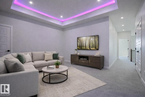 Living area featuring a tray ceiling with recessed lighting and accent lighting, light-colored carpeting, and a wall-mounted television - Rural Leduc County, AB - Indoor Photo Showing Living Room