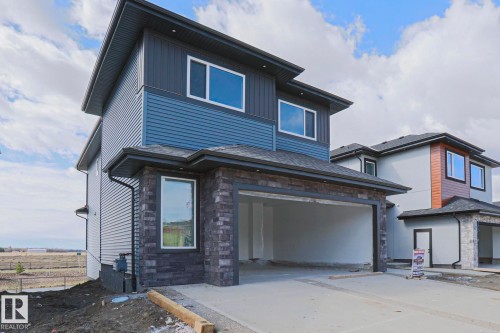 The property features a modern exterior with blue and dark grey siding, stone accents, and an integrated garage - Rural Leduc County, AB - Outdoor