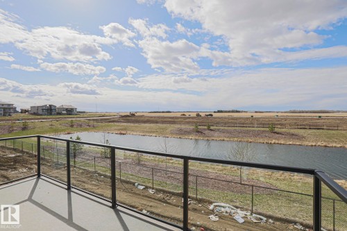 This property features a balcony with a glass railing, offering views of a pond and open fields - Rural Leduc County, AB - Outdoor With View