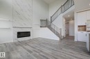 The property features a spacious living area with light-toned flooring, a tall fireplace with a marble-style finish, and a staircase with dark metal railings - Rural Leduc County, AB  - Indoor With Fireplace 