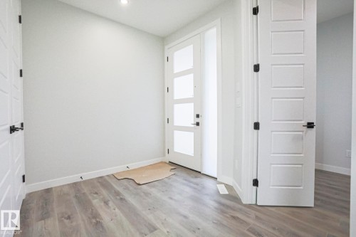 Entryway featuring light gray wood-style flooring, white walls, and a contemporary front door with translucent glass panels - Rural Leduc County, AB - Indoor Photo Showing Other Room