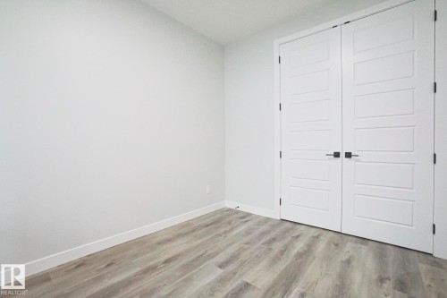 This room features light-colored walls, contemporary white double doors with dark hardware, and light wood-look flooring - Rural Leduc County, AB - Indoor Photo Showing Other Room