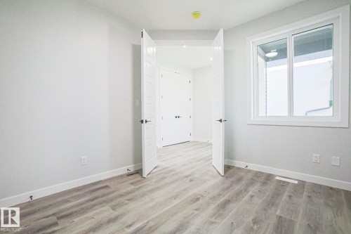The property features light-colored laminate flooring and a white window with a view of an exterior wall - Rural Leduc County, AB - Indoor Photo Showing Other Room