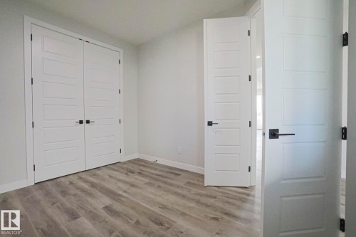This room features light grey walls, grey wood-look flooring, and white doors with matte black hardware - Rural Leduc County, AB - Indoor Photo Showing Other Room