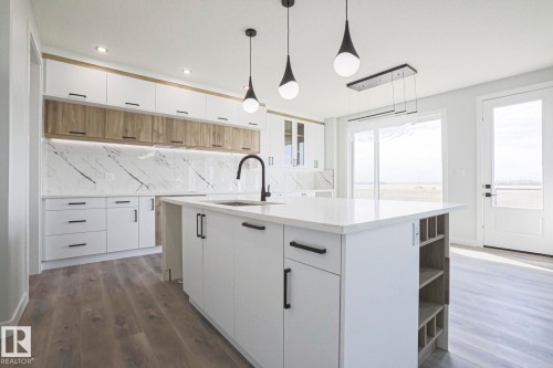 The kitchen features modern white cabinetry, a large island with a countertop, and a white marble-patterned backsplash - Rural Leduc County, AB - Indoor Photo Showing Kitchen With Upgraded Kitchen