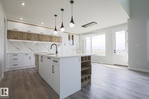 Modern kitchen featuring white cabinetry, a large island with a sink, pendant lighting, and a view of the outdoors through expansive windows and a glass-paneled door - Rural Leduc County, AB - Indoor Photo Showing Kitchen