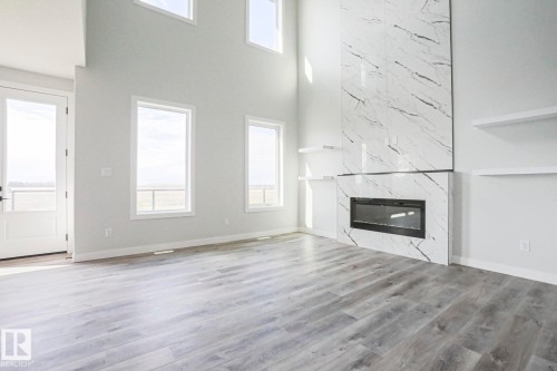 The main living area features high ceilings, wide plank flooring, and a contemporary fireplace with a large format marble surround - Rural Leduc County, AB - Indoor With Fireplace