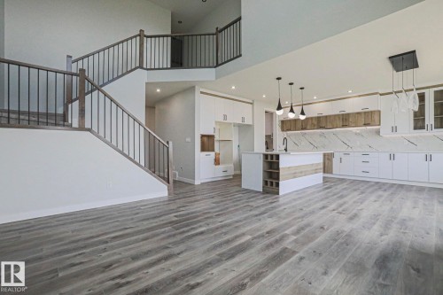 This property features an open-concept living space with light-toned hardwood flooring and a modern kitchen - Rural Leduc County, AB - Indoor