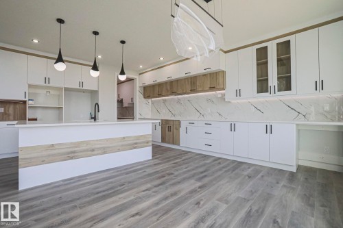 Modern kitchen featuring a spacious island with a sink and contemporary pendant lighting, white cabinetry with wood accents, and striking marble-patterned backsplashes - Rural Leduc County, AB - Indoor Photo Showing Kitchen With Upgraded Kitchen