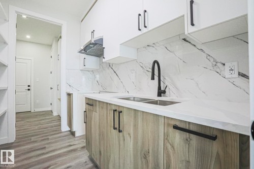 The kitchen features white upper cabinetry, wood-look lower cabinetry, and a white countertop - Rural Leduc County, AB - Indoor Photo Showing Kitchen With Double Sink With Upgraded Kitchen