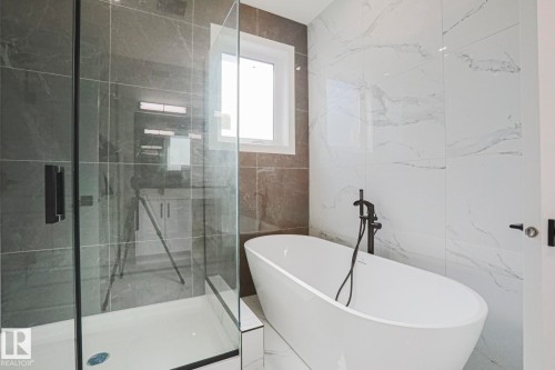 The bathroom features a freestanding soaking tub with a matte black floor-mounted faucet, a glass-enclosed shower with a dark tiled wall, and white wall tiles with natural veining - Rural Leduc County, AB - Indoor Photo Showing Bathroom