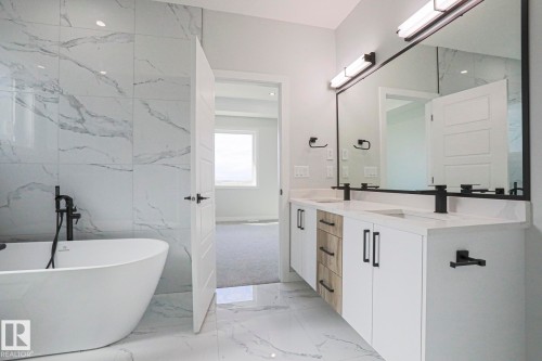 This contemporary bathroom features a freestanding soaking tub, a double vanity with stone countertops and undermount sinks, and a large mirror with integrated lighting - Rural Leduc County, AB - Indoor Photo Showing Bathroom
