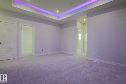 This spacious room features light-colored carpeting, white walls, and a tray ceiling with recessed lighting and accent lighting - Rural Leduc County, AB - Indoor Photo Showing Other Room