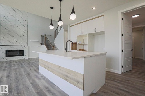 Open concept living space featuring a kitchen island with a white countertop and a black faucet, white cabinetry, and recessed lighting - Rural Leduc County, AB - Indoor With Fireplace