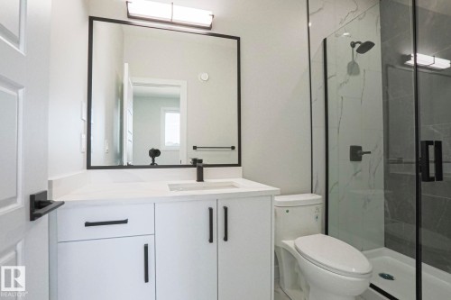 This bathroom features a contemporary vanity with a white countertop and dark hardware, a framed mirror, and a glass-enclosed shower with dark fixtures and patterned tile - Rural Leduc County, AB - Indoor Photo Showing Bathroom