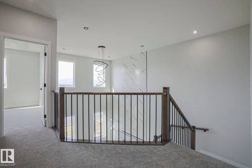 The property features a staircase with a dark wood banister and black metal spindles, leading to a carpeted landing - Rural Leduc County, AB - Indoor Photo Showing Other Room