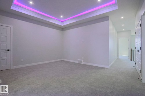 This room features plush carpet flooring and a tray ceiling with recessed lighting and accent lighting - Rural Leduc County, AB - Indoor Photo Showing Other Room