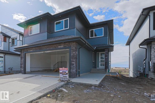 The property features a two-story exterior with dark blue siding and stone accents, a concrete driveway leading to an integrated garage, and a modern front door with frosted glass panels - Rural Leduc County, AB - Outdoor