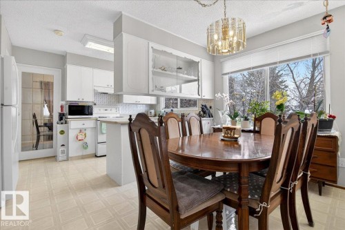 Kitchen and dining area featuring white cabinetry, a kitchen island, and a large window providing views of trees - 391 Lee Ridge Road, Edmonton, AB - Indoor Photo Showing Dining Room