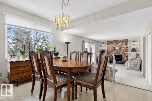 Dining space featuring a large window, a decorative chandelier, and a view of the living area with a brick fireplace - 391 Lee Ridge Road, Edmonton, AB - Indoor Photo Showing Dining Room With Fireplace