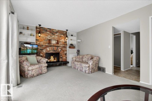 The living room features a brick fireplace with an arched opening, flanked by built-in shelving units - 391 Lee Ridge Road, Edmonton, AB - Indoor Photo Showing Other Room With Fireplace