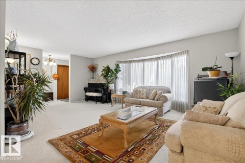 The living room features light-colored carpeting, light grey walls, and a large bay window with vertical blinds - 391 Lee Ridge Road, Edmonton, AB - Indoor Photo Showing Living Room