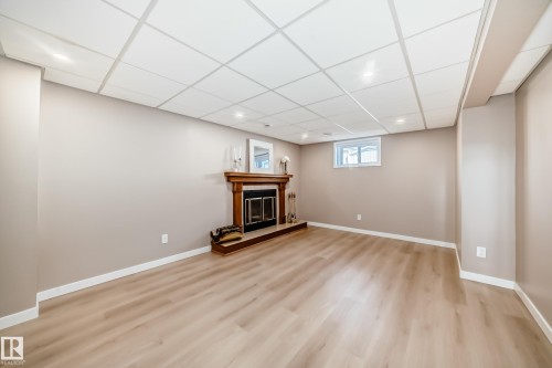 Spacious room featuring light-toned flooring, neutral painted walls, and a fireplace with a wooden mantel - 287 Lago Lindo Crescent, Edmonton, AB - Indoor Photo Showing Basement