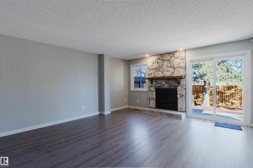 Spacious living area featuring stone fireplace, wood mantle, recessed lighting, and sliding glass doors to the outdoors - 17308 61 Avenue, Edmonton, AB - Indoor Photo Showing Living Room With Fireplace