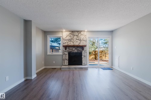Living area featuring light gray walls, wood-look flooring, a stone fireplace with a dark wood mantel, and sliding glass doors that open to the outside - 17308 61 Avenue, Edmonton, AB - Indoor Photo Showing Living Room With Fireplace