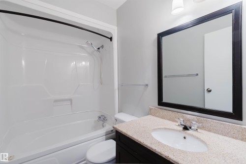 Bathroom featuring a bathtub with an integrated shower, a vanity with a light-colored countertop, and a framed mirror - 17308 61 Avenue, Edmonton, AB - Indoor Photo Showing Bathroom