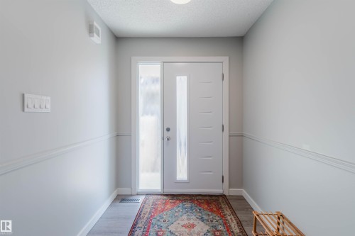 The entrance features a white door with vertical glass panels and a sidelight, complemented by light grey walls and a patterned area rug over light wood flooring - 17308 61 Avenue, Edmonton, AB - Indoor Photo Showing Other Room