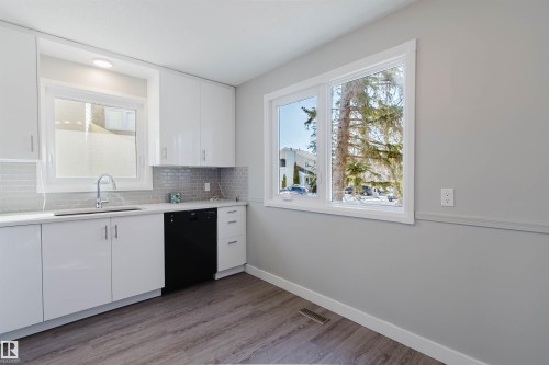 The kitchen features white cabinetry with sleek handles, a stainless steel sink with a gooseneck faucet, and a black dishwasher - 17308 61 Avenue, Edmonton, AB - Indoor Photo Showing Kitchen