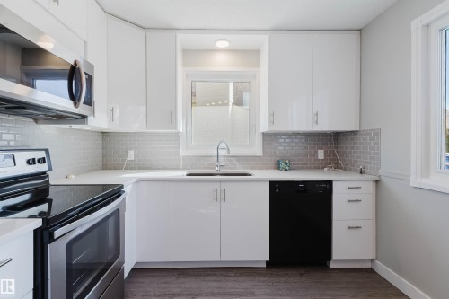 The kitchen features white cabinetry, light-colored countertops, a tile backsplash, and stainless steel appliances - 17308 61 Avenue, Edmonton, AB - Indoor Photo Showing Kitchen