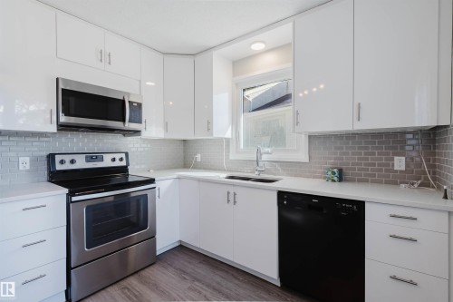 The kitchen features white cabinetry, stainless steel appliances, a grey subway tile backsplash, and a double basin sink - 17308 61 Avenue, Edmonton, AB - Indoor Photo Showing Kitchen With Stainless Steel Kitchen With Double Sink With Upgraded Kitchen