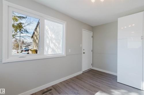 This space features a large window, a white door, and white floor-to-ceiling cabinetry, all complemented by light-colored walls and wood-look flooring - 17308 61 Avenue, Edmonton, AB - Indoor Photo Showing Other Room