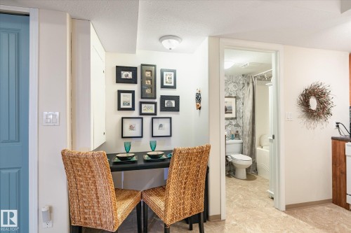 This property features a dining area with a wall-mounted table and two woven chairs, situated near a light blue paneled door - 5 4902B 43 Street, Legal, AB 