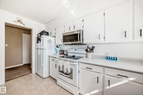 The kitchen features white cabinetry with black hardware, a stainless steel microwave, and a white refrigerator - 11323 162 Avenue, Edmonton, AB - Indoor Photo Showing Kitchen