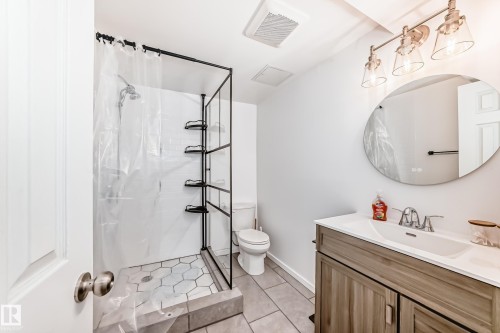 The bathroom features a modern vanity with a rectangular sink, a circular mirror, and a shower with hexagonal floor tiles - 11323 162 Avenue, Edmonton, AB - Indoor Photo Showing Bathroom