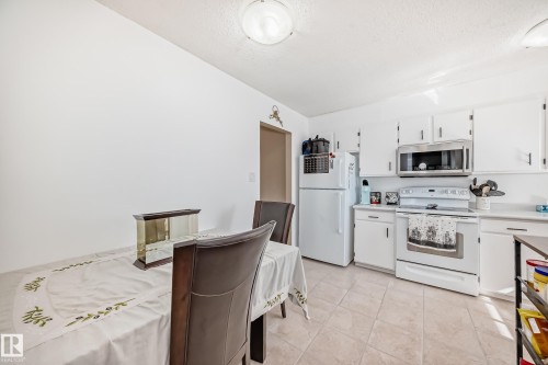 The kitchen features white cabinetry, a white refrigerator, and a white stove with a stainless steel microwave - 11323 162 Avenue, Edmonton, AB - Indoor Photo Showing Kitchen