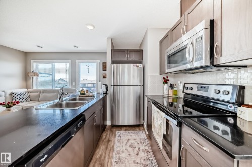 The kitchen features stainless steel appliances, including a microwave, refrigerator, and range - 11 1530 Tamarack Boulevard, Edmonton, AB - Indoor Photo Showing Kitchen With Double Sink With Upgraded Kitchen