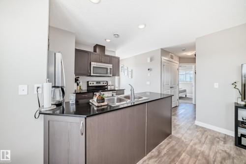 The kitchen features dark wood cabinetry, stainless steel appliances, a double sink, and a large central island with a dark countertop - 11 1530 Tamarack Boulevard, Edmonton, AB - Indoor Photo Showing Kitchen With Double Sink
