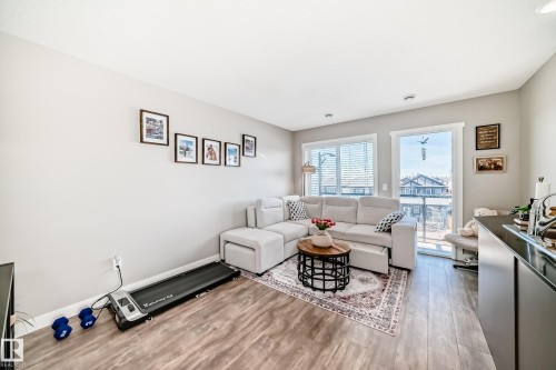 The living area features wood-style flooring, light-colored walls, and large windows providing natural light - 11 1530 Tamarack Boulevard, Edmonton, AB - Indoor Photo Showing Living Room