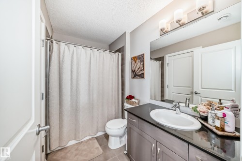 Bathroom featuring a vanity with a dark countertop and an oval sink, a large wall-mounted mirror, and a shower with a light-colored curtain - 11 1530 Tamarack Boulevard, Edmonton, AB - Indoor Photo Showing Bathroom