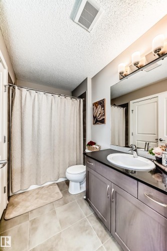 The bathroom features a vanity with a dark countertop and an integrated sink, a toilet, and tiled flooring - 11 1530 Tamarack Boulevard, Edmonton, AB - Indoor Photo Showing Bathroom