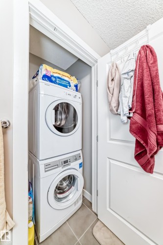This utility area features a stacked washer and dryer unit, set within a dedicated alcove - 11 1530 Tamarack Boulevard, Edmonton, AB - Indoor Photo Showing Laundry Room