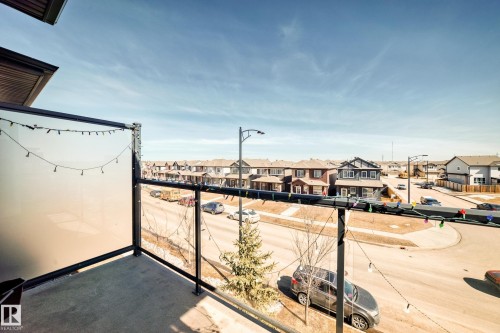 The property features a balcony with a frosted glass privacy panel and metal railings, offering views of the surrounding neighborhood and clear skies - 11 1530 Tamarack Boulevard, Edmonton, AB - Outdoor With Balcony